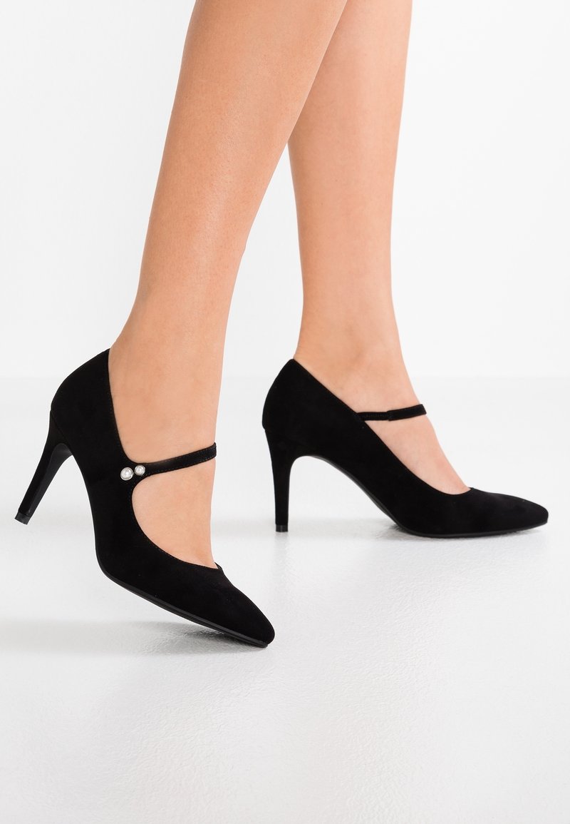 Des chaussures à talons hauts en suède noir présentent un bout pointu, une fine bride de cheville et deux accents décoratifs en perles sur le côté.