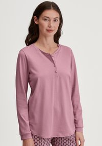 Langarmige roze top met een knoopsluiting bij de hals. Zachte textuur, relaxte pasvorm en contrasterende manchetten. Gecombineerd met een pantalon met een patroon.