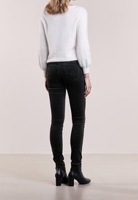 Černé skinny džíny s vysokým pasem, jemnými zadními kapsami a hladkým povrchem. Spárováno s bílým, nadýchaným svetrem a černými botami na podpatku.