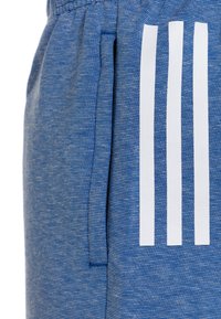 Blå sportshorts i strukturerad tyg, med en framficka och tre vita vertikala ränder på sidopanelen.