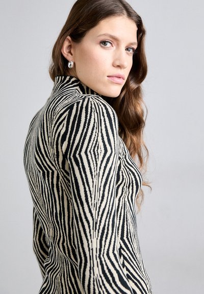 Μπλούζα με τσέπη ζέβρας σε μαύρο και μπεζ χρώμα με εφαρμοστή σχεδίαση και υφή πλεκτού. Καθαρές, καθορισμένες γραμμές και λεία υφή.