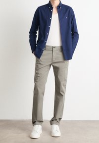 Chemise bleu marine boutonnée sur un débardeur blanc, associée à un pantalon gris clair et des baskets blanches. Tissu lisse avec coupe classique et détails.
