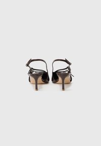 Sandali con tacco alto in pelle verniciata nera, con cinghie alla caviglia, punta affusolata e tacco stiletto sottile. Suola texturizzata con una finitura beige.