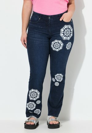 Pantalon en denim bleu foncé avec des motifs floraux en dentelle blanche sur les jambes. Dispose d'une taille mi-haute et d'un design classique à cinq poches.