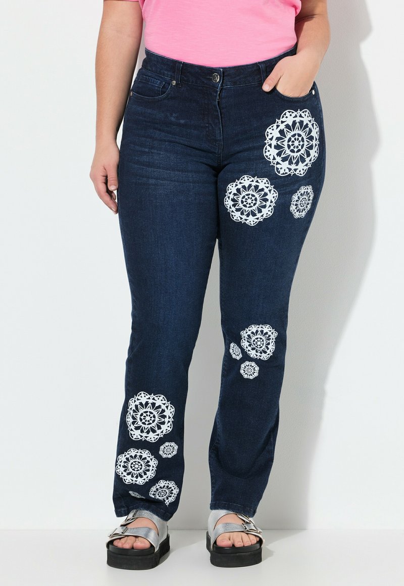 Pantalones de mezclilla de un azul oscuro con patrones florales de encaje blanco en las piernas. Cuenta con una cinturilla de talle medio y un diseño clásico de cinco bolsillos.