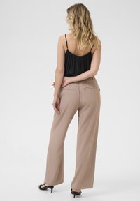 Beige pantalons met brede pijpen, een gladde textuur en een op maat gemaakt ontwerp, gecombineerd met een zwarte tanktop en zwarte hoge hakken.