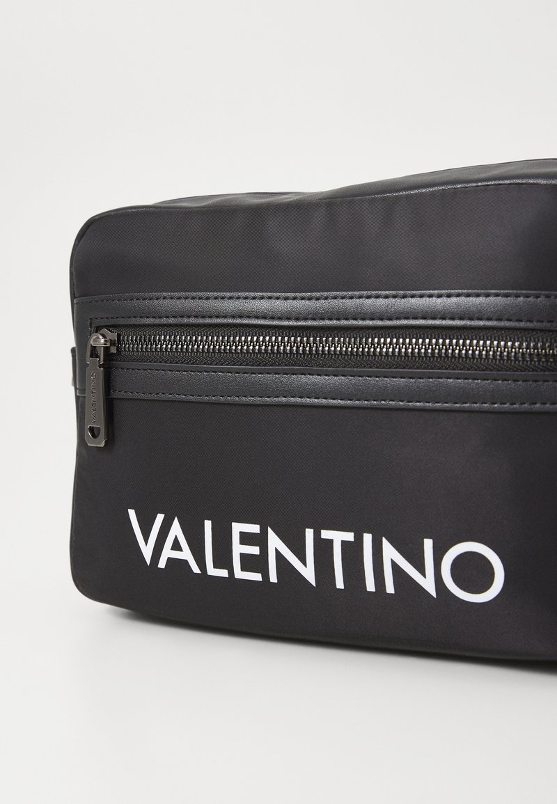 Sac en nylon noir avec un logo "VALENTINO" blanc bien visible, une texture lisse et une fermeture éclair noire contrastante avec des éléments de marque.
