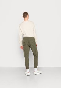 Olivgröna cargobyxor med resårmidja, två bakfickor och förstärkta knäsektioner, som bärs med vita sneakers och strumpor.