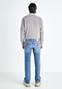 Camisa gris de manga larga con cuello redondo, combinada con jeans de denim azul claro de corte estándar y bolsillos traseros con detalles de costura.