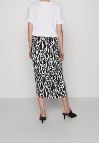 Jupe midi à imprimé léopard noir et blanc avec une silhouette élégante, une texture lisse et une fente sur le côté, portée avec un t-shirt blanc uni.