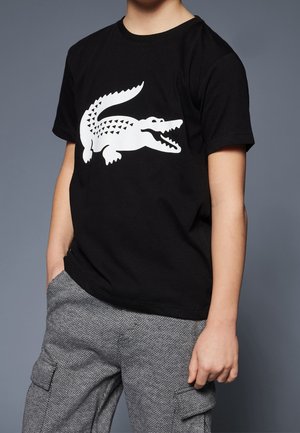 Czarny bawełniany t-shirt z dużym białym graficznym wizerunkiem krokodyla. Krótkie rękawy i okrągły dekolt. W zestawie ze wzorzystymi, szarymi spodniami cargo.