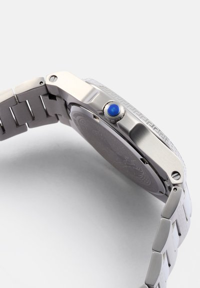 Reloj de acero inoxidable plateado con una correa texturizada, corona con acento azul y fondo grabado. Presenta un diseño de caja cuadrada y robusta.