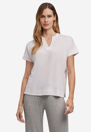 Haut blanc à manches courtes avec un col en V et une coupe décontractée. Le tissu semble doux avec une texture lisse, stylé avec des ourlets roulés.