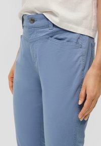 Pantalones de color azul claro hechos de una tela suave, con cierre de botón y bolsillos laterales; ajuste entallado con detalles de costura visibles.