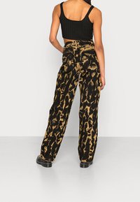 Schwarz-goldene Batik-weitbeinige Jeans mit hoher Taille, sichtbar genäht und mit zwei Gesäßtaschen, kombiniert mit einem schwarzen ribbed Cropped Top.