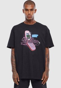 Sort t-shirt med et grafisk motiv af en pink vintage mobiltelefon og teksten "Hotline" i fed skrift. Lavet af bomuldsstof, afslappet pasform.
