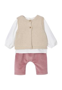 Beige gestrickte Weste mit zwei Knöpfen, die über einem weißen Langarmshirt getragen wird, kombiniert mit pinken Cordhose mit abgerundetem Saum.