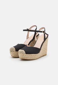 Zapatos de cuña negros con una base de cuerda trenzada y punta redonda. Cuenta con una parte superior de tela negra, tira en el tobillo y plantilla de color rosa claro.