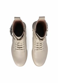 Stivaletti in pelle beige alla caviglia con design con lacci, zip laterale e accento in fibbia metallica. Texture liscia con punta rotonda e tacco basso.
