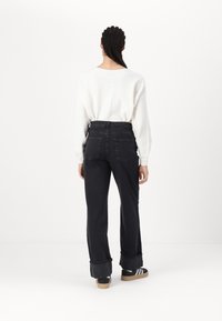 Black denim trousers with a high waist, rolled cuffs, two back pockets, paired with a white knit sweater, viewed from the back.