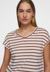 Gestreept T-shirt in wit en bruin, met een v-hals, korte mouwen en een klein accentlogo op de borst. Zachte stoftextuur.