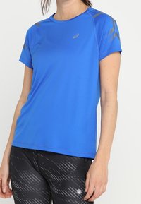 Modré atletické tričko s krátkým rukávem a kulatým výstřihem, s šedými akcenty na ramenou a materiálem odvádějícím vlhkost pro aktivní nošení.