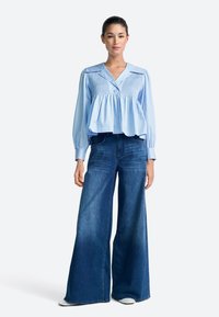 Világoskék, gombos blúz smock díszítéssel az elején és széles ujjakkal, sötétkék, magasderekú, bőszárú farmernadrággal párosítva.
