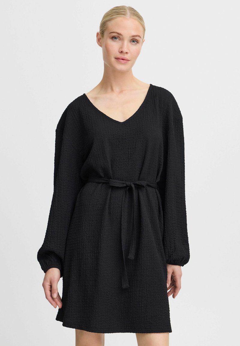 Robe noire en tissu texturé, présentant un décolleté en V, des manches longues et une ceinture nouée à la taille pour un ajustement réglable.