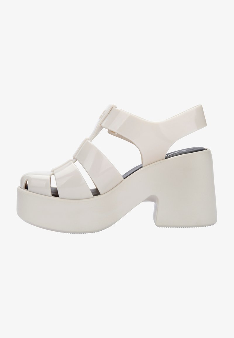 Sandales à plateforme blanches avec une finition brillante, présentant des larges brides, une ouverture à l'avant et un talon épais. Semelle plate pour la stabilité.