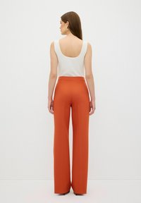 Witte geribde tanktop met een diepe rug, gecombineerd met hoge taille roest-oranje wijde broek. Glad textuur; minimale details.
