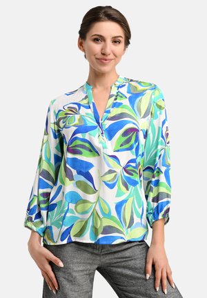 Bunte Bluse mit floralem Muster in Grün- und Blautönen, aus leichtem Stoff, mit V-Ausschnitt und Dreiviertelärmel, kombiniert mit grauen Hosen.