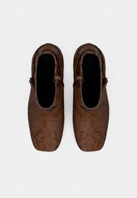 Zapatos de patrón de serpiente marrón con un diseño elegante, superficie texturizada, punta redondeada y un pequeño detalle de hebilla en el lado.