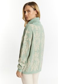 Mint green sweater with a textured floral pattern in light tan, featuring a high collar and ribbed cuffs. Soft knit fabric with a relaxed fit.