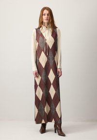 Dolga obleka brez rokavov z geometrijskim vzorcem diamantov v odtenkih bordo rdeče, bež in sive. Obleka ima stranski razporek in gladko teksturo.