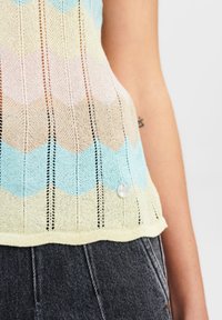 Sweter dziergany z falistym wzorem w pastelowych kolorach (niebieski, żółty, beżowy) z pionowymi paskami i detalem w postaci perłowego guzika na dolnym wykończeniu.