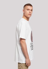 Bílý bavlněný tričko s kulatým potiskem s textem "LOST TUNE". Krátké rukávy, volný střih a klasický kulatý výstřih.