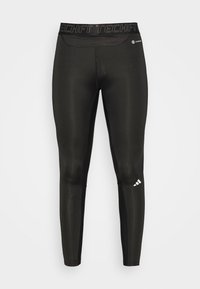 Leggings deportivos negros con una textura suave, forma ajustada y una cintura alta con "TECHFIT" en negro. Detalle del logo en la parte inferior de la pierna.