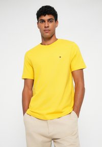 Κίτρινο κοντομάνικο μπλουζάκι από βαμβάκι με στρογγυλή λαιμόκοψη. Διαθέτει ένα μικρό λογότυπο στην αριστερή περιοχή του στήθους. Απλός σχεδιασμός, χωρίς μοτίβα.