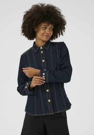 Chemise en denim foncé avec des boutons dorés, des coutures verticales, un col et des manches longues avec des poignets à boutons.