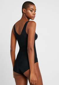 Μαύρο κορμάκι με φαρδιές τιράντες, στενή σιλουέτα και αδιάσπαστο σχέδιο, διαθέτοντας ομαλή υφή και κλασικό λαιμόκομμα με δέσιμο στον λαιμό.