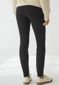 Svarta leggings med en åtsittande design, slät textur och midjehög midja, matchade med vita sneakers och en ljusfärgad tröja.