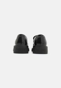 Chaussures en cuir verni noir avec un bout arrondi, semelle épaisse en caoutchouc noir, et logo "TOMMY JEANS" en relief sur le talon.