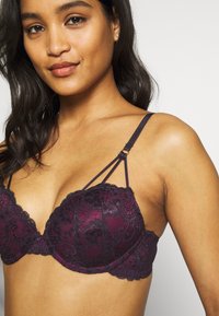 Paarse kanten bh met een gewatteerd onderdraadontwerp; heeft bloemenpatronen, verstelbare bandjes en decoratieve hardwareaccenten.