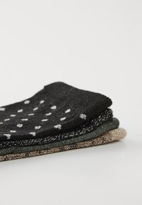 Tres pares de calcetines: uno negro con lunares blancos, uno verde oscuro y uno beige o dorado, todos con un material texturizado y brillante.
