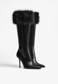 Čierne kožené vysoké čižmy po kolená s umelou kožušinou na vrchu, s ostrou špičkou a štíhlym siluetou.