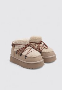 Bottes chevilles beige avec tige duveteuse, lacets texturés et semelle plateforme épaisse. Dotées d'œillets ronds et d'une finition douce semblable à de la laine.
