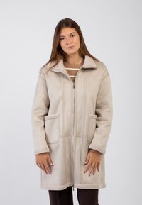 Cappotto beige con zip, dalla texture morbida, dotato di colletto e polsini foderati in pelliccia, dettagli di cucitura verticale e due tasche sul fronte.