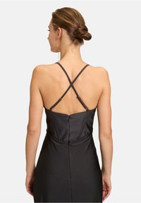 Czarna sukienka z dopasowanym gorsetem, skrzyżowanymi ramiączkami i zapięciem na zamek z tyłu. Gładka tekstura, zaprojektowana dla uzyskania smukłej sylwetki.