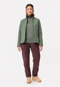 Lichte groene geïsoleerde jas met ritszakken, gecombineerd met een getailleerde groene top en kastanjebruine broek. Gedragen met tan wandelhoge schoenen.