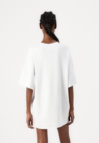 Bijela oversized majica od mekog materijala. Ima kratke rukave i okrugli izrez. Jednostavan dizajn bez vidljivih uzoraka ili logotipa.